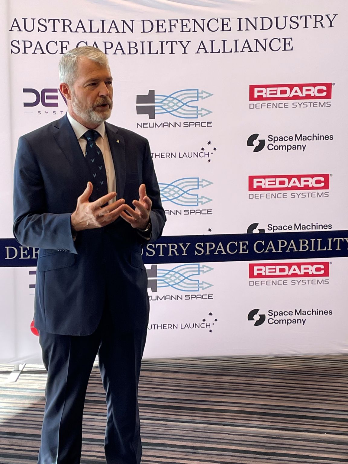 Speaker in front of the Australian Defence Industry Space Capability Alliance banner at the 13th Australian Space Forum